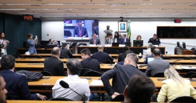 Audiência pública em plenário com participantes, painel de monitoramento e apresentação de fatos.