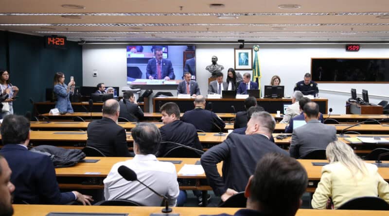 Audiência pública em plenário com participantes, painel de monitoramento e apresentação de fatos.